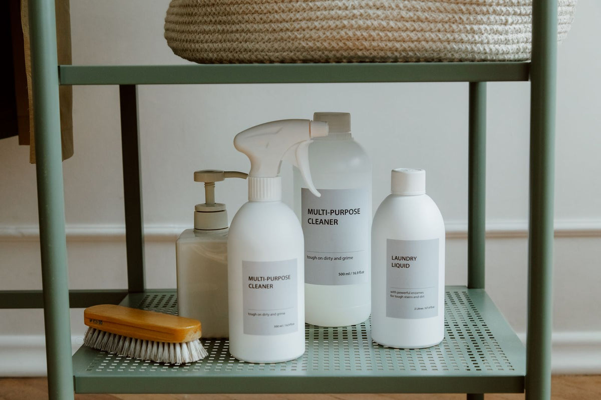 Refillable cleaning bottles and a natural bristle brush on a green shelf