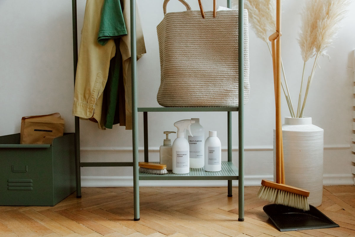 Sage green shelf with woven baskets and natural cleaning bottles in a calm, tidy home